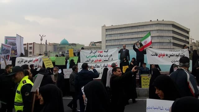 Crowd of Iranians demonstrating in a city street, holding banners and an Iranian flag.