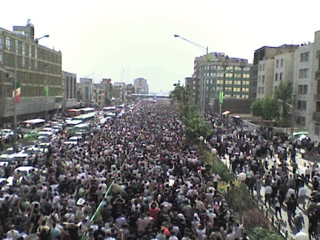 Massive crowd of protestors fills a city street with buildings lining both sides.