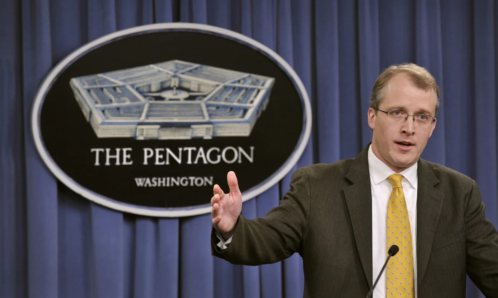 George E. Little, Pentagon Press Secretary, briefing the media at a podium.