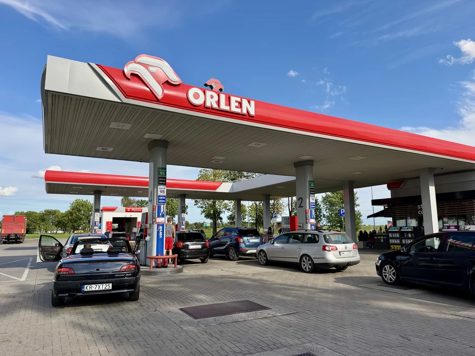 Vehicles parked at fuel pumps under the red canopy of an Orlen gas station.