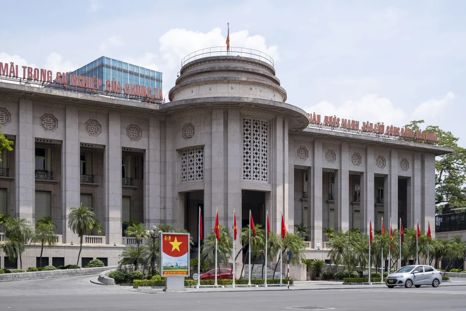 The State Bank of Vietnam building with flags and a banner on a sunny day.