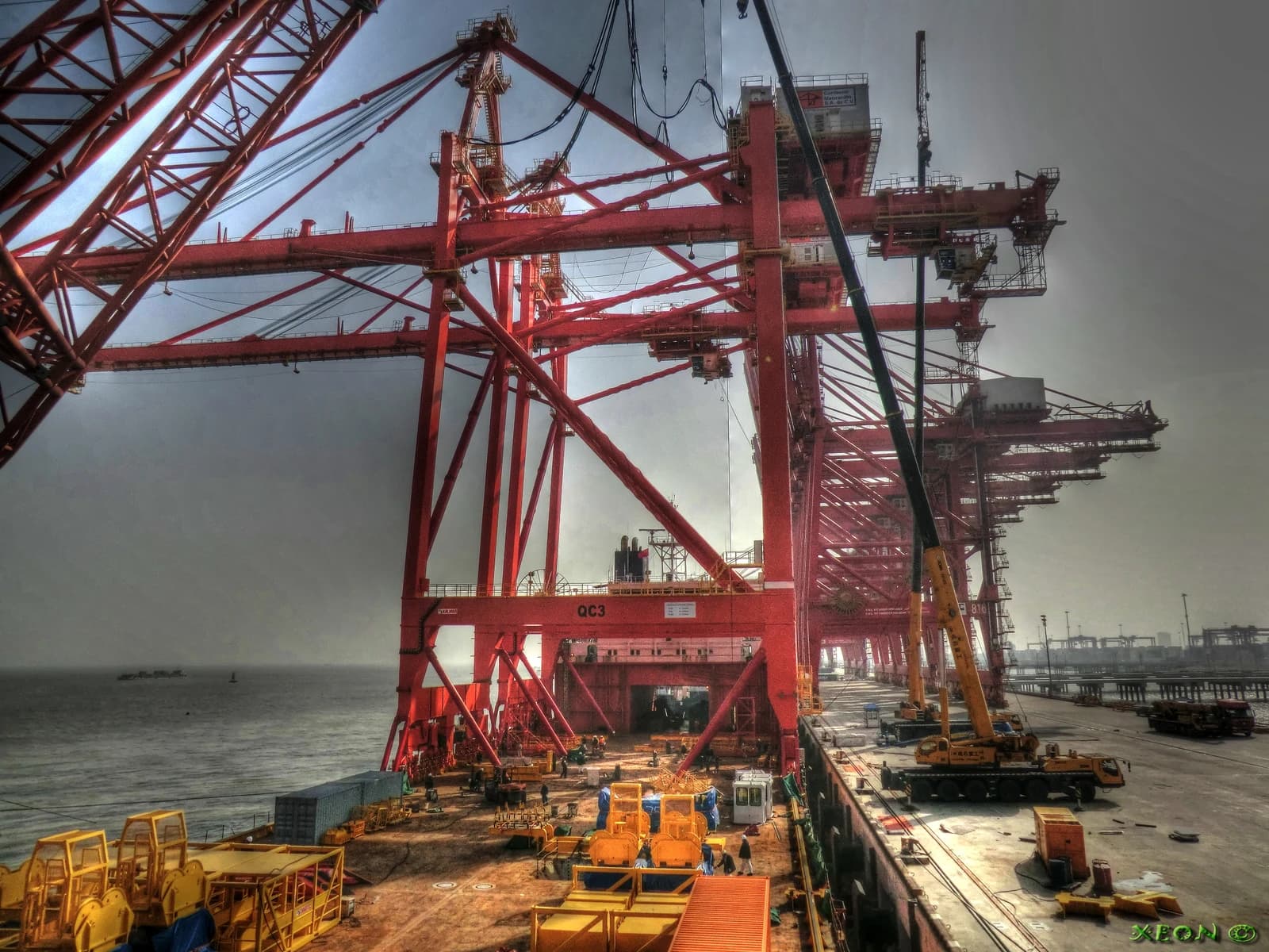 Large red container cranes on a dock next to a cargo vessel.