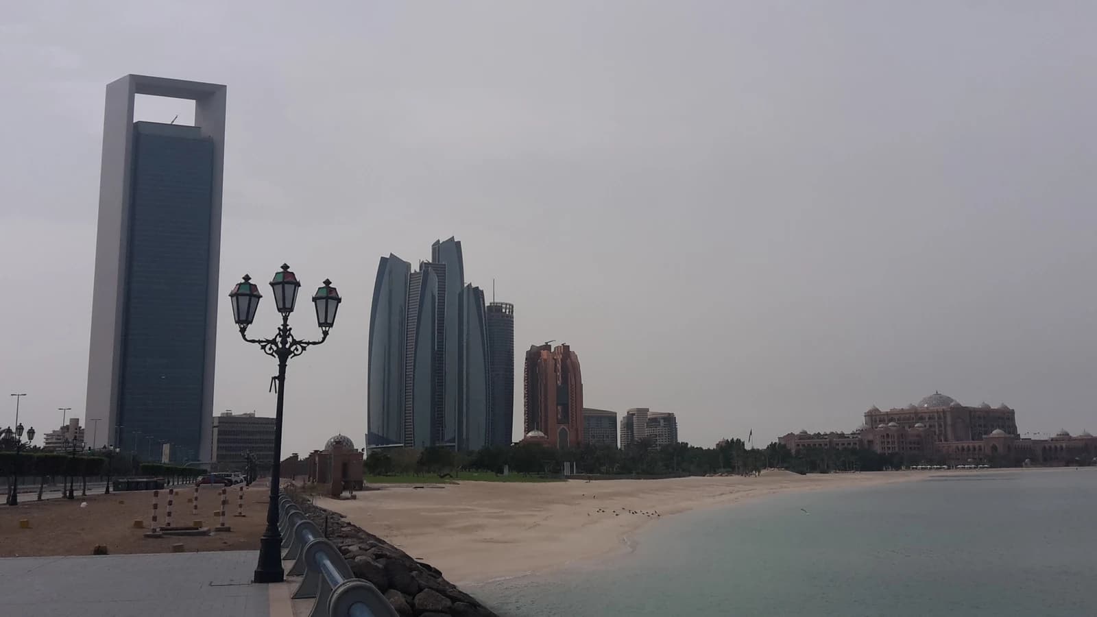 Abu Dhabi skyline features various tall buildings and a long sandy beach along the water.