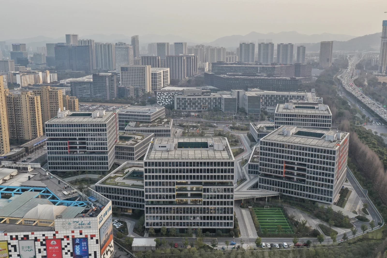 Aerial view of Alibaba Center buildings in Binjiang, Hangzhou, China, with city and mountains in background.