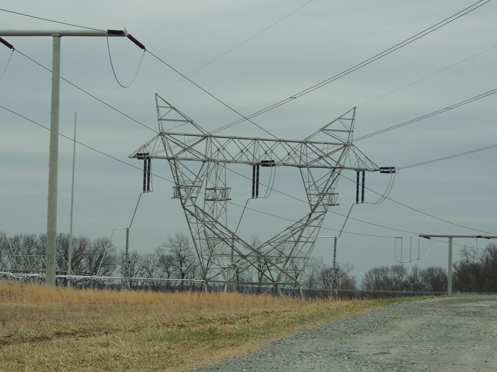 Electricity transmission tower, power lines, and substation equipment under a cloudy sky.