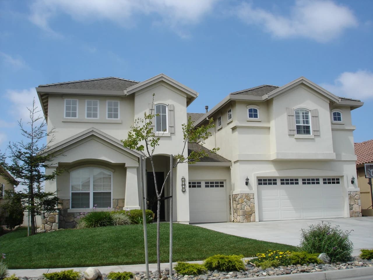 Suburban tract house with a light stucco exterior and multiple garage doors on a sunny day.
