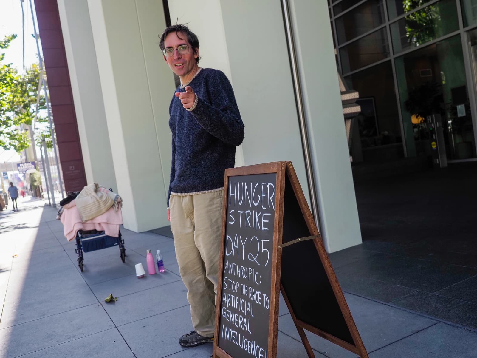 Guido Reichstadter, anti-AI protester, points at the camera next to a sign about a hunger strike.