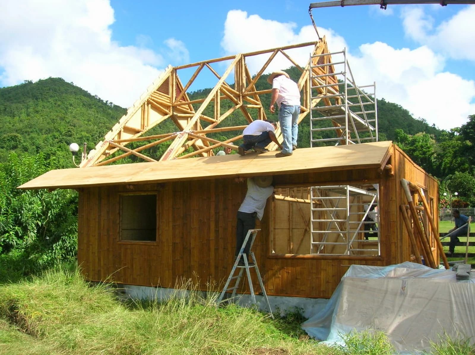 Workers constructing the roof and frame of a bamboo house in a natural setting.