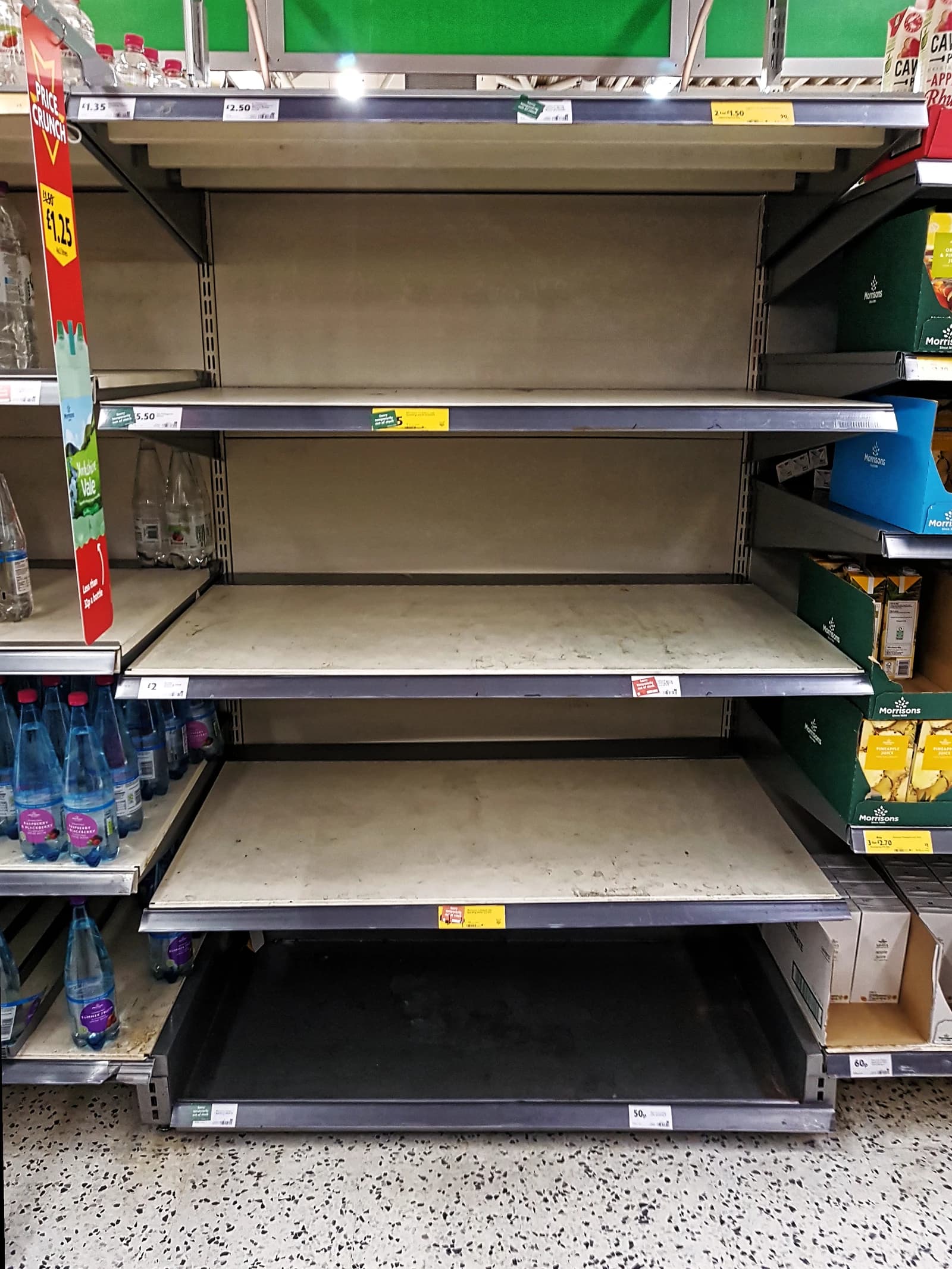 Empty shelves in a Morrisons supermarket, with some bottles remaining on the lower shelves.