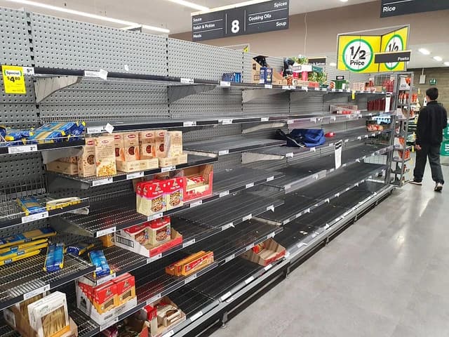 Empty dried pasta shelves in an Australian supermarket with a lone shopper.