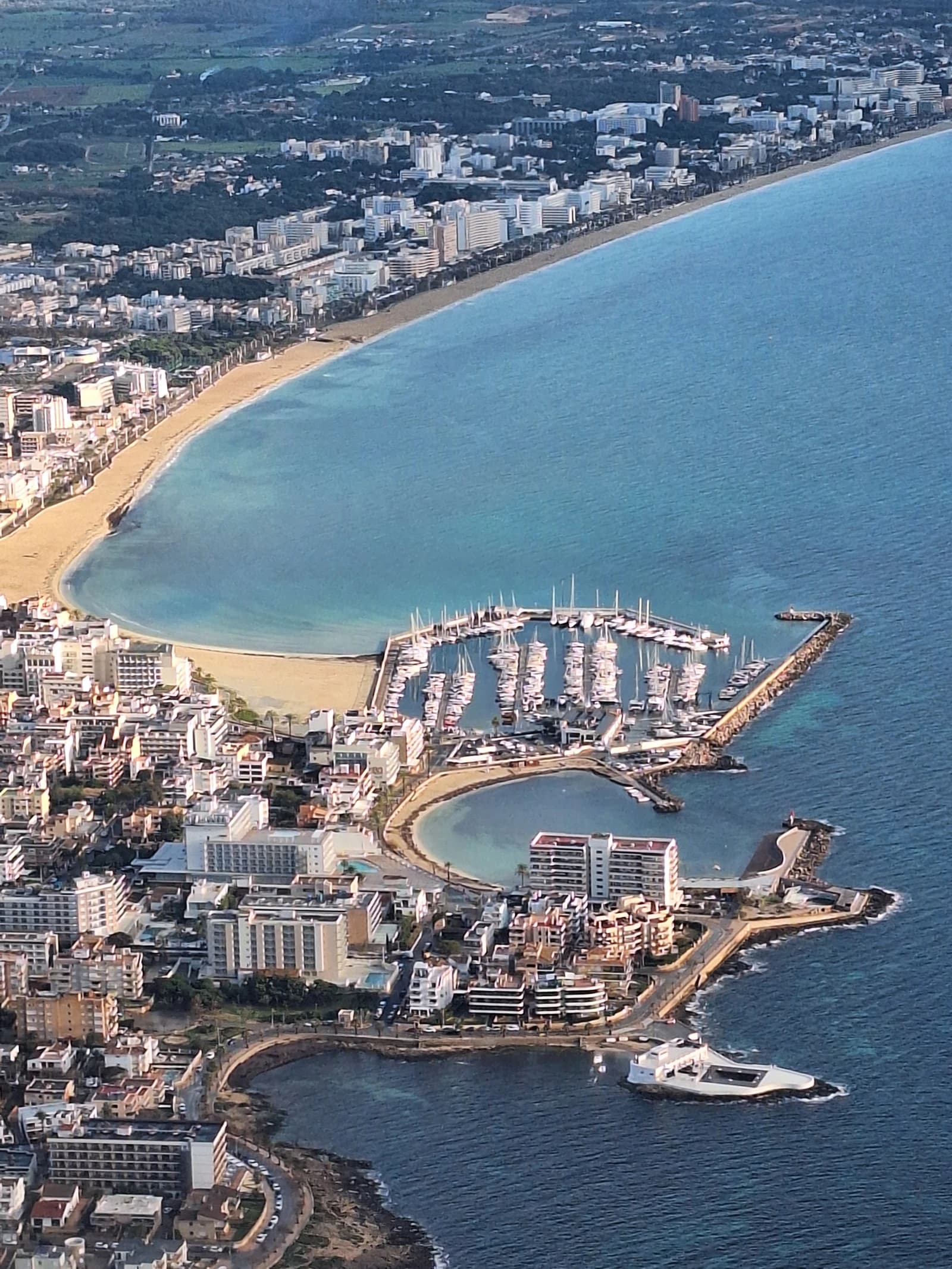 Aerial view of a coastal town with a marina full of boats, beaches, and buildings.
