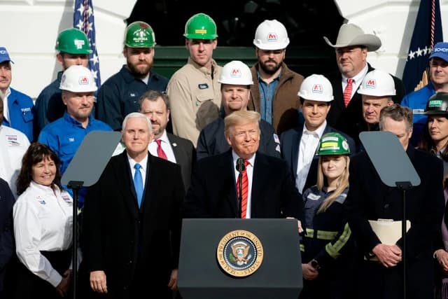 Donald Trump speaks at a podium with the Seal of the President, Vice President Mike Pence stands beside him.