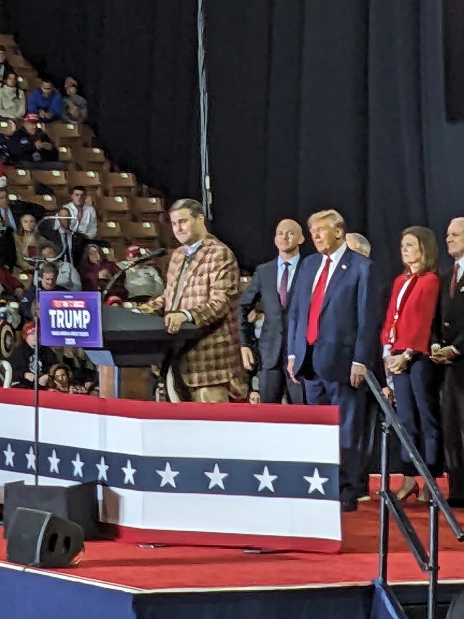 Donald Trump, former President, standing on a stage with other people.