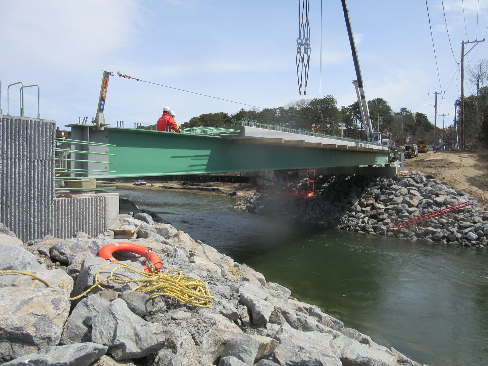 Construction workers building a new bridge over a body of water with heavy machinery.