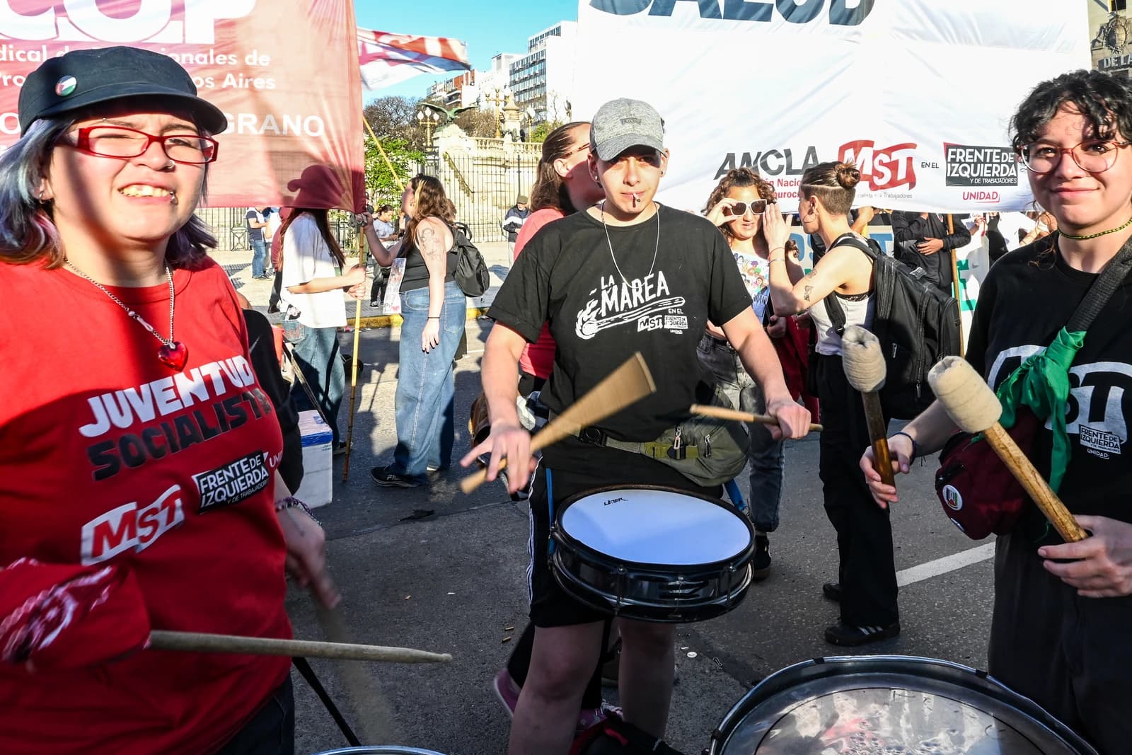 People playing drums at a protest in Argentina, with banners visible in the background.