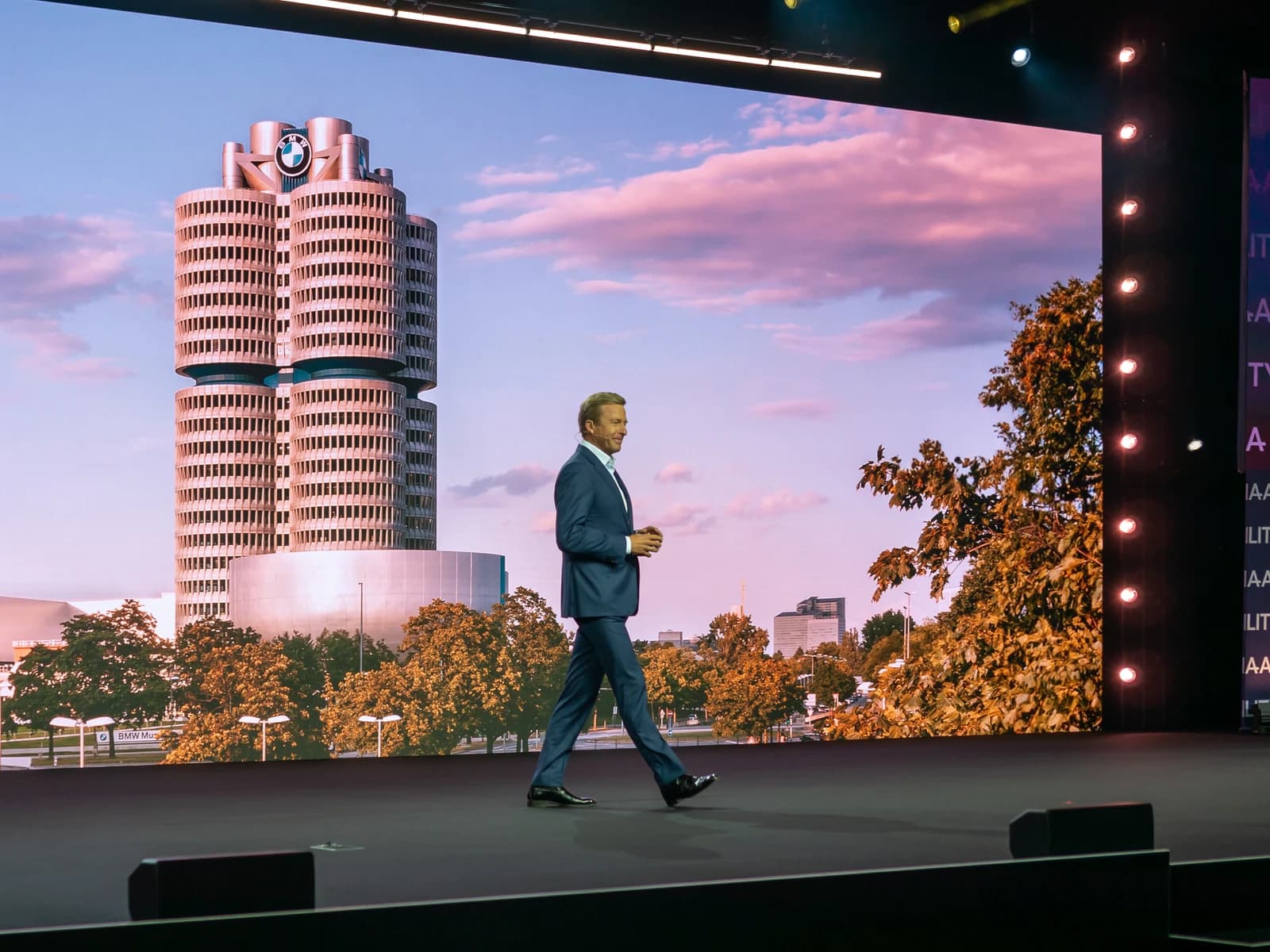 Man in suit walks on stage with BMW Headquarters projected behind him.