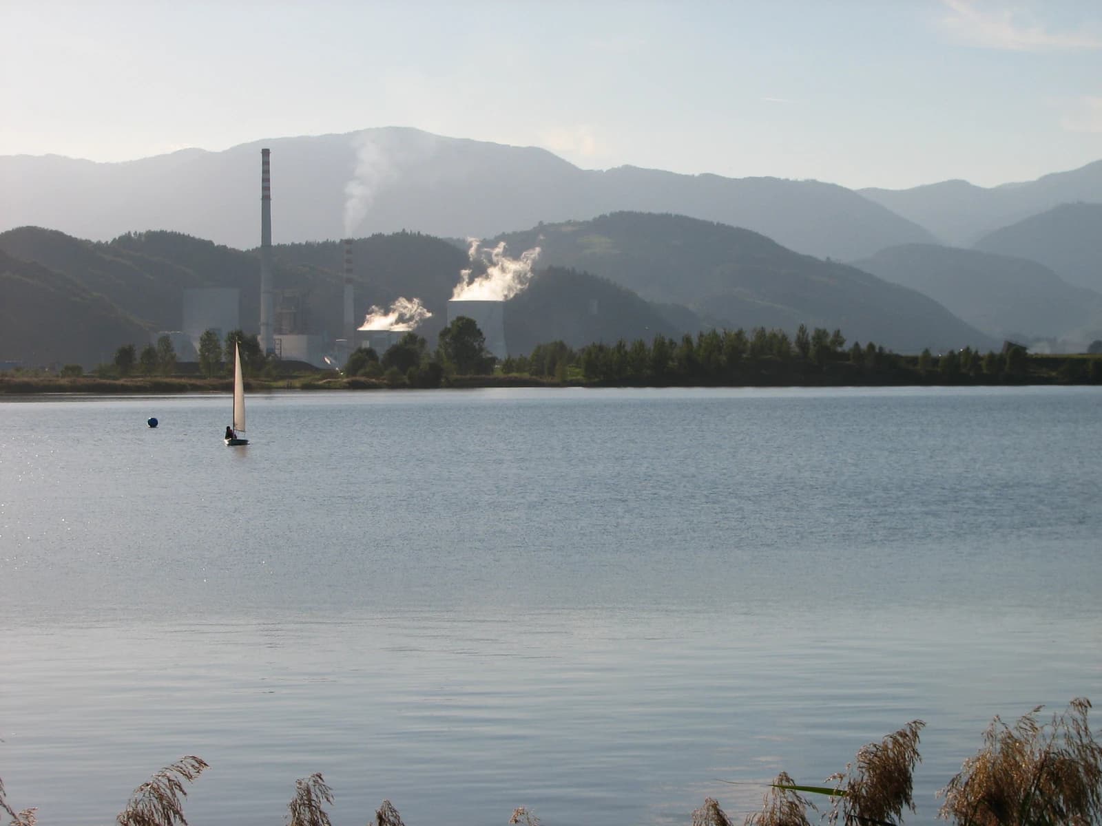Velenje Lake with Šoštanj Thermal Power Plant and mountains in the background.