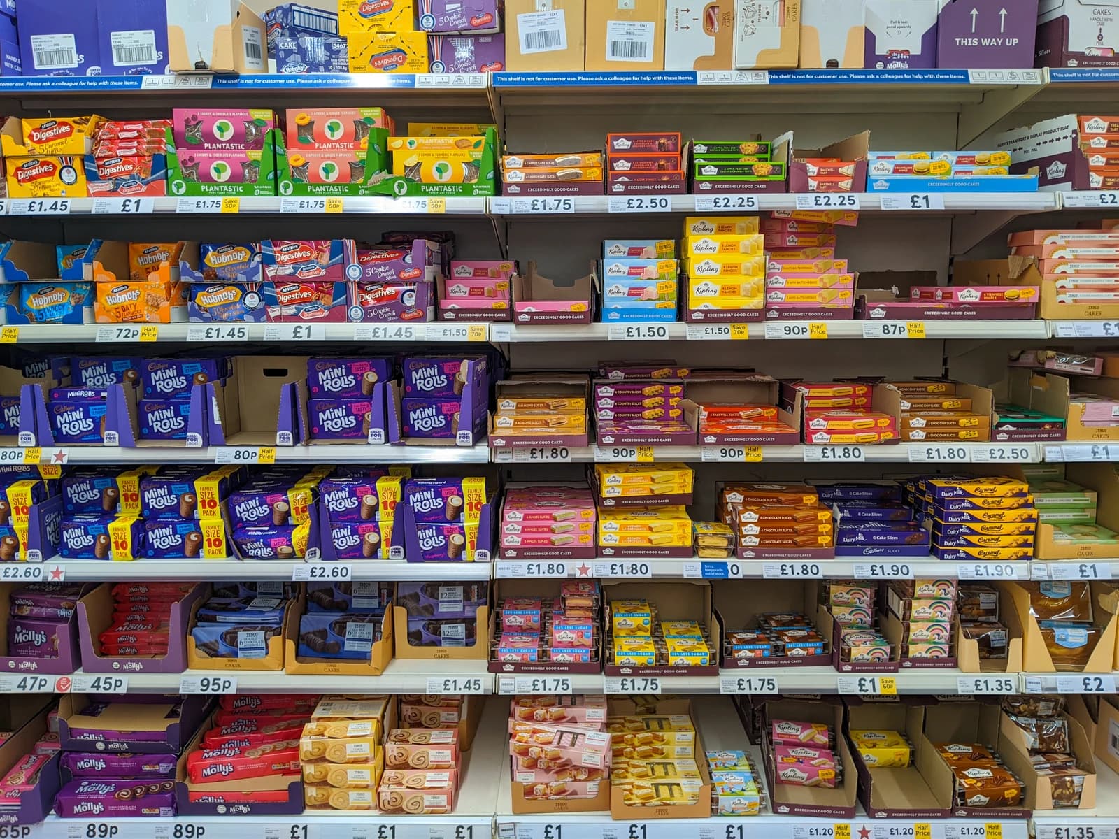Rows of packaged cakes, cookies, and biscuits on shelves with price tags in a supermarket aisle.