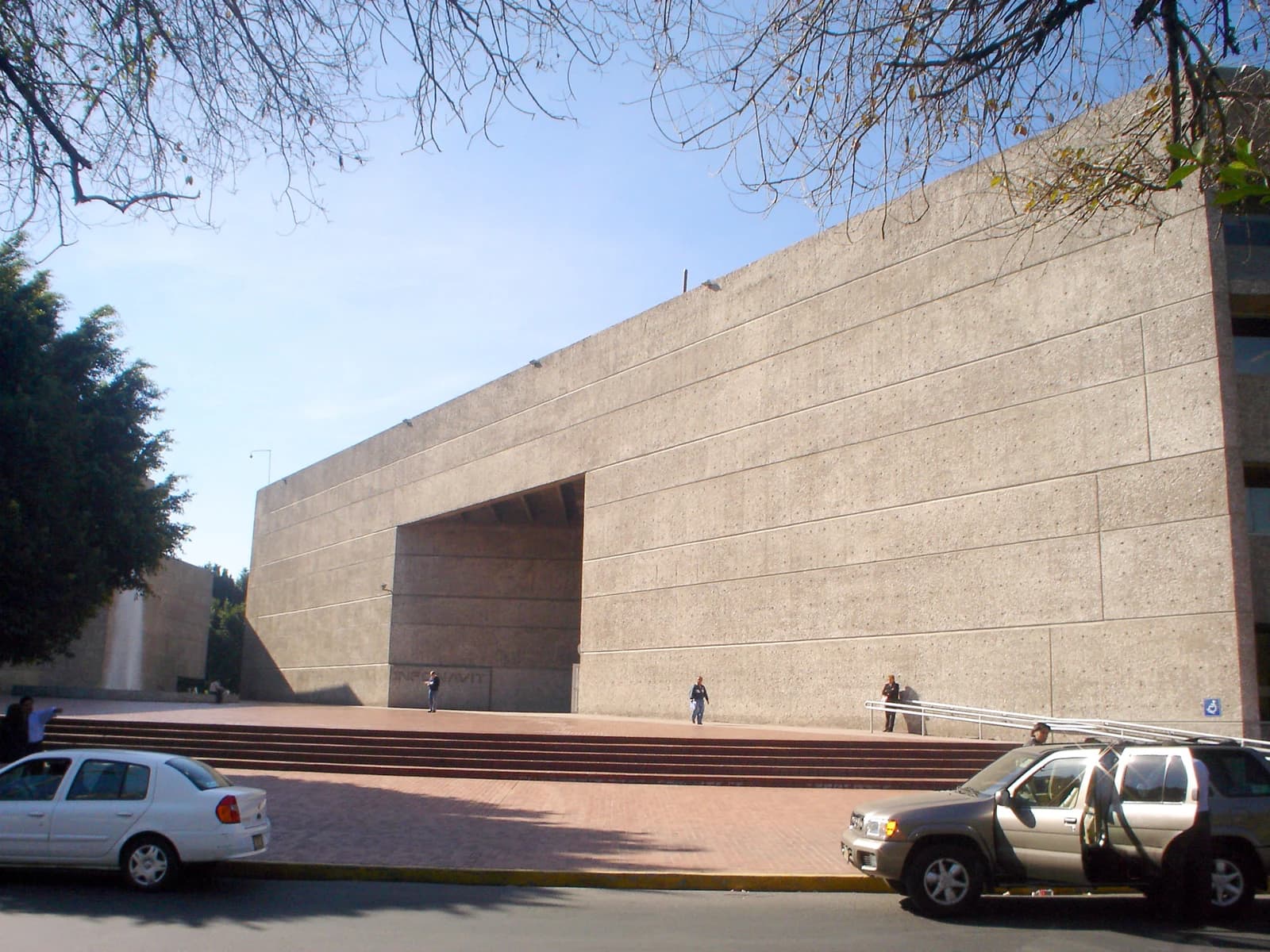Exterior view of the Infonavit building in Mexico, with cars parked and people walking.