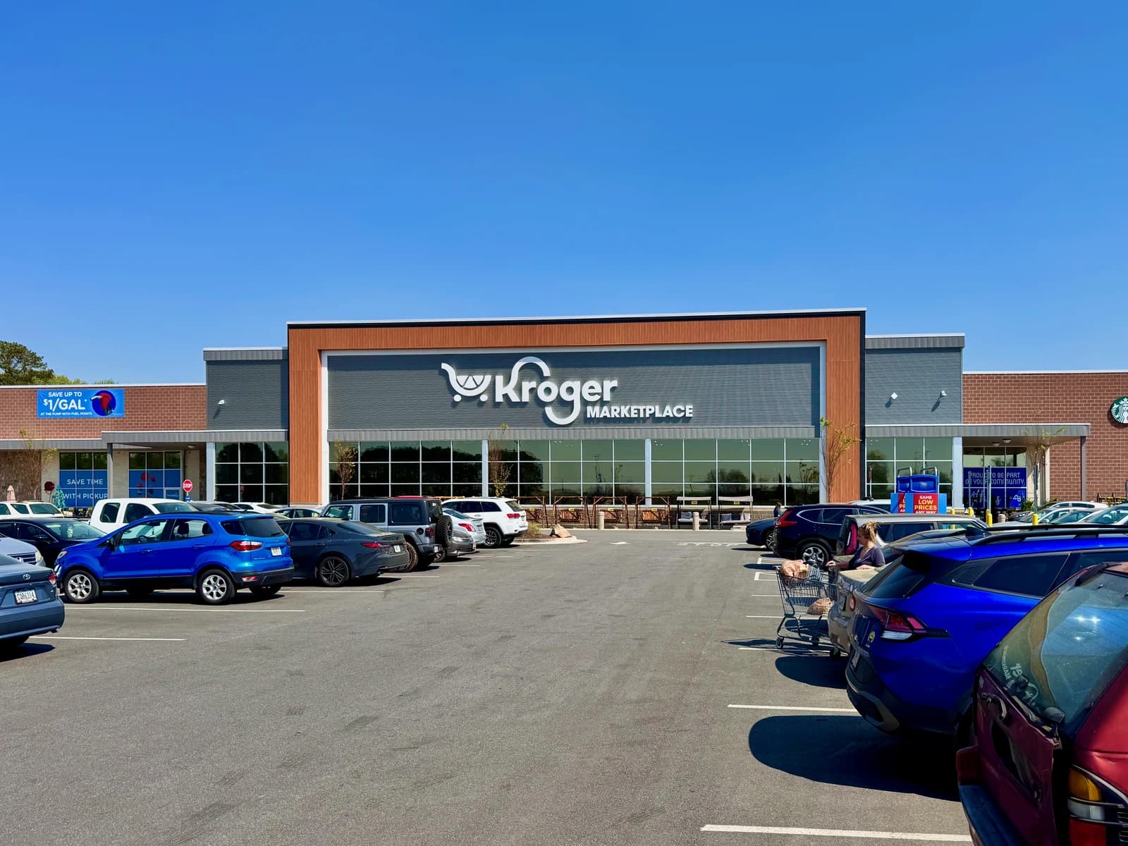 Exterior of a Kroger Marketplace grocery store building with a parking lot full of cars.