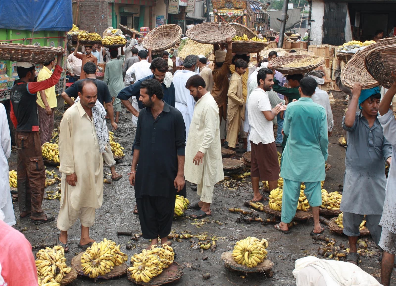 Men carrying baskets of bananas and standing in a busy market in Pakistan.