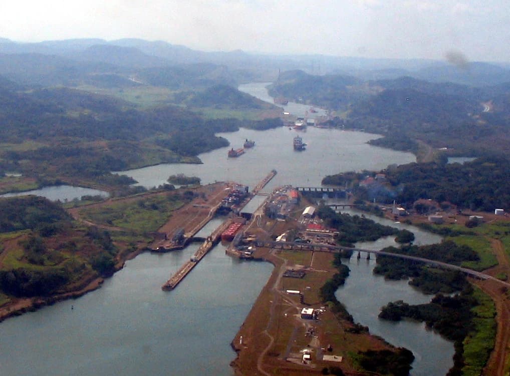 Aerial view shows the Miraflores Locks of the Panama Canal, with ships and surrounding landscape.