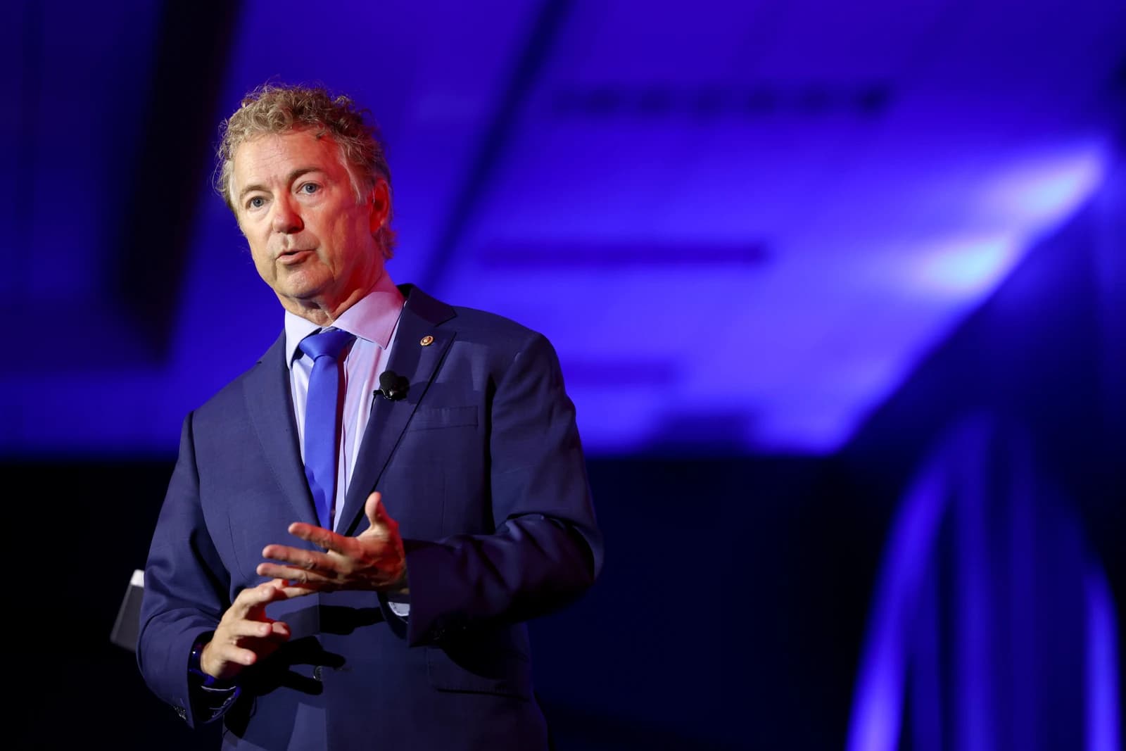 U.S. Senator Rand Paul speaking at a podium with a blue background.
