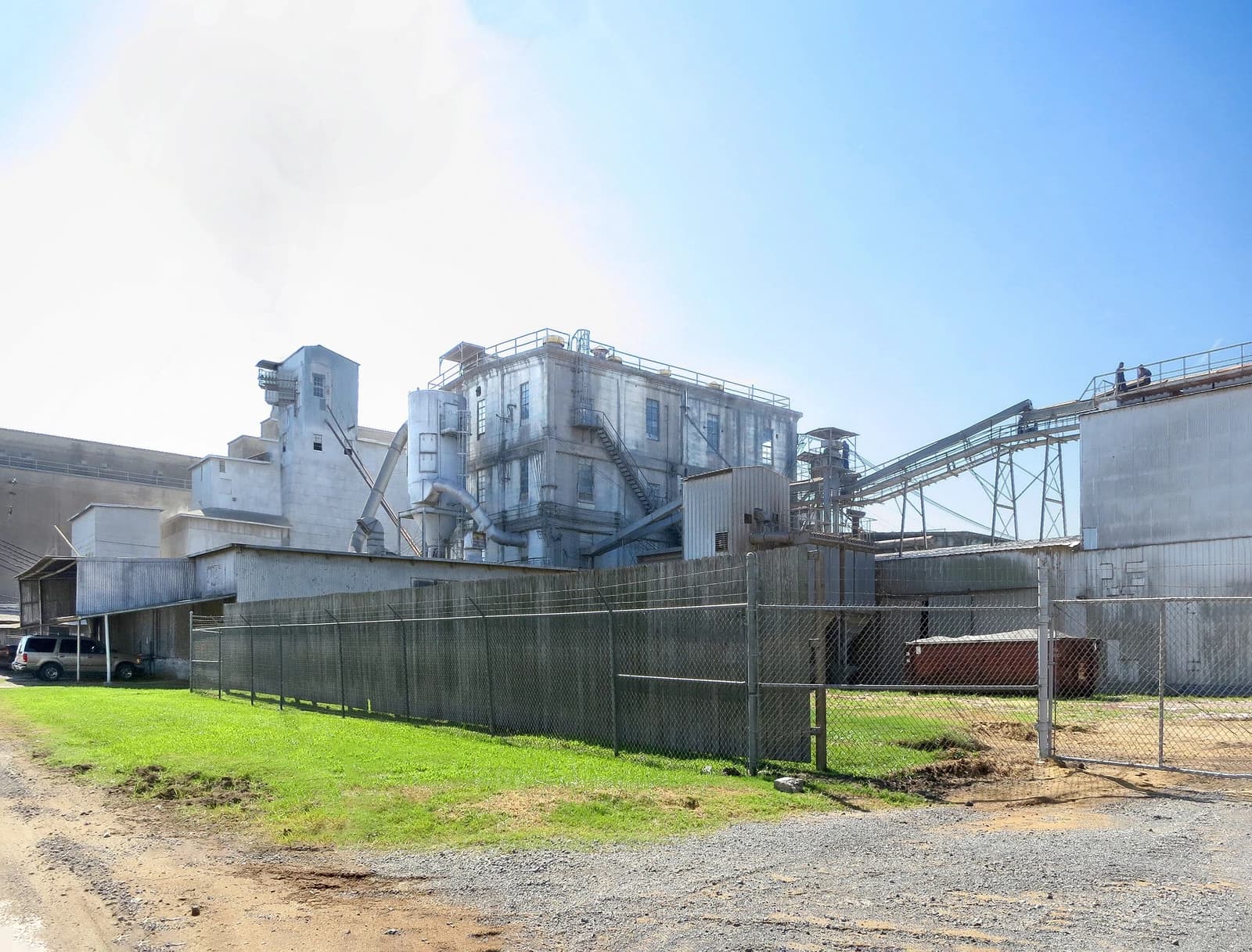 Exterior view of a large industrial complex with multiple buildings and conveyer belts.