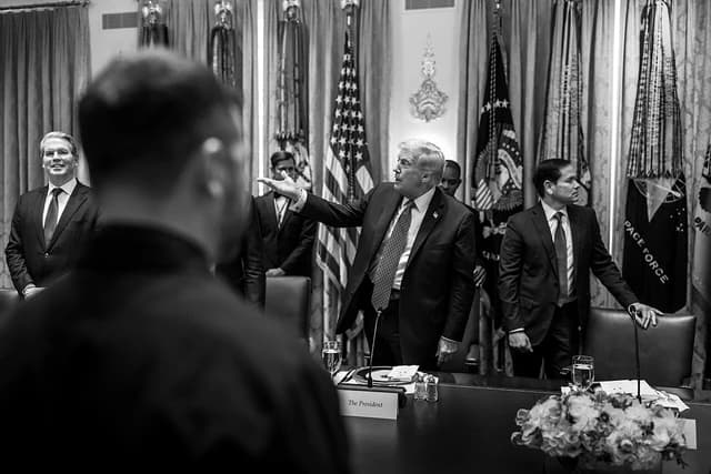Donald Trump gestures while speaking in a room with other men in suits.