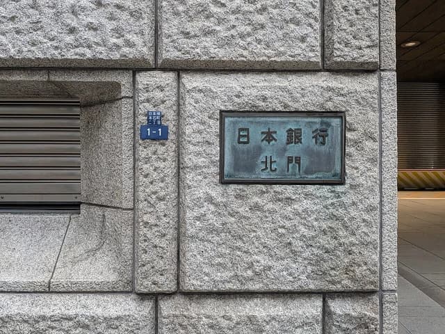 Plaque with Japanese characters 'Bank of Japan North Gate' on a rough stone wall.