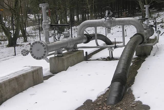 An outdoor gas pipeline system with pipes and valves, partially covered in snow.