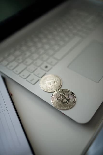 Two silver Bitcoin coins rest on a light-colored laptop keyboard next to a notepad.