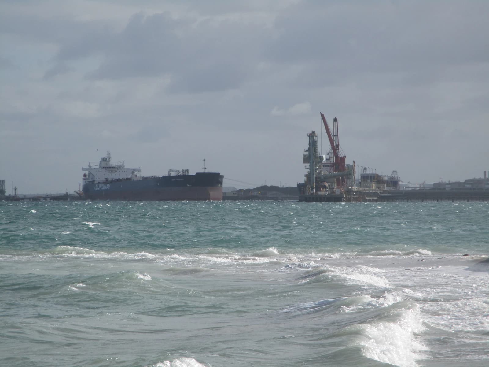 An oil tanker named Euronav docked at an oil refinery jetty with cranes.