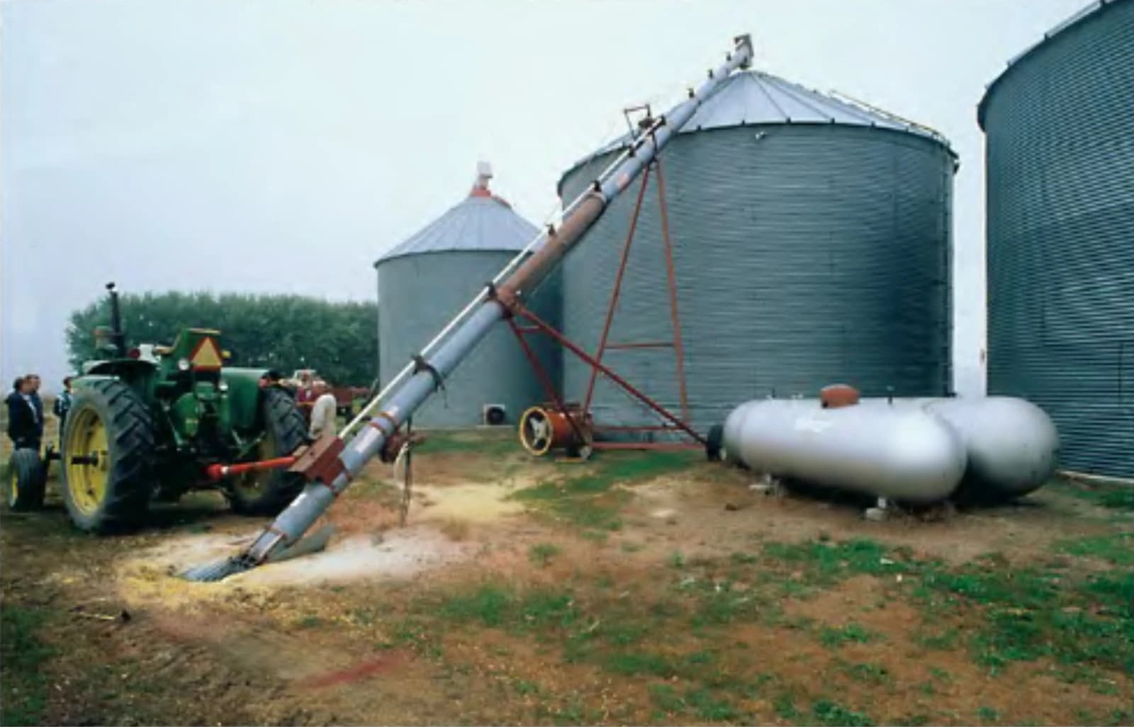 Tractor unloading corn onto an auger that leads to a grain silo.