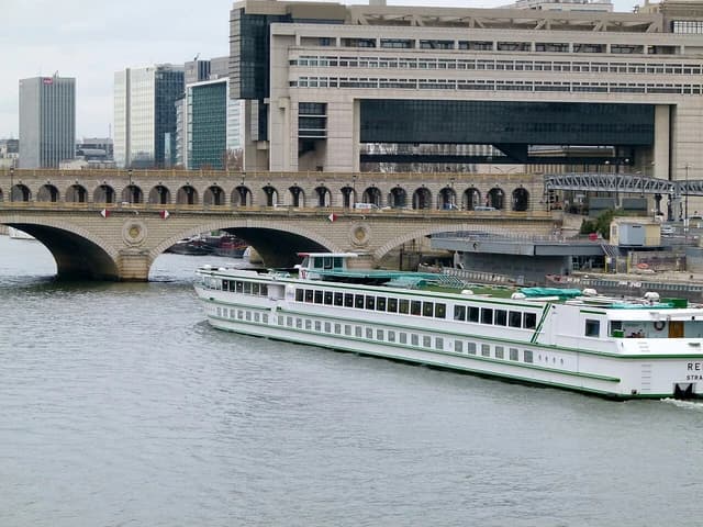 Bercy Ministry of Finance building in Paris with a bridge and a boat on the river.