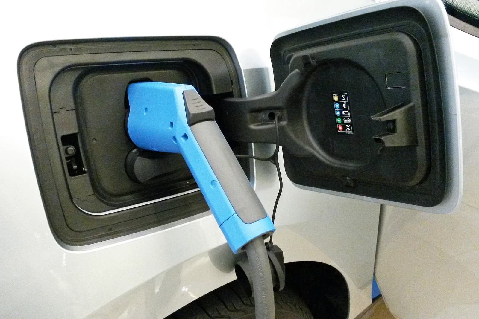 Blue charging plug inserted into the charging port of a white electric car.