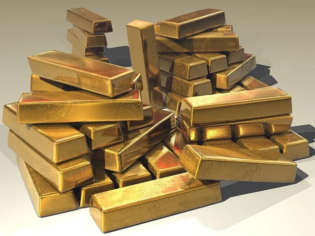 Numerous shiny gold bullion bars stacked and piled together.