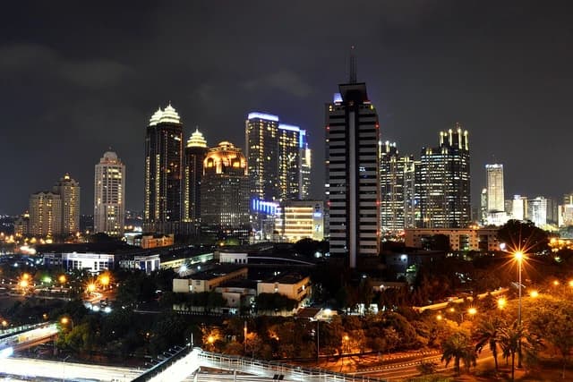 Skyline of Sudirman Central Business District (SCBD) in Jakarta at night, with illuminated buildings and streaking car lights.
