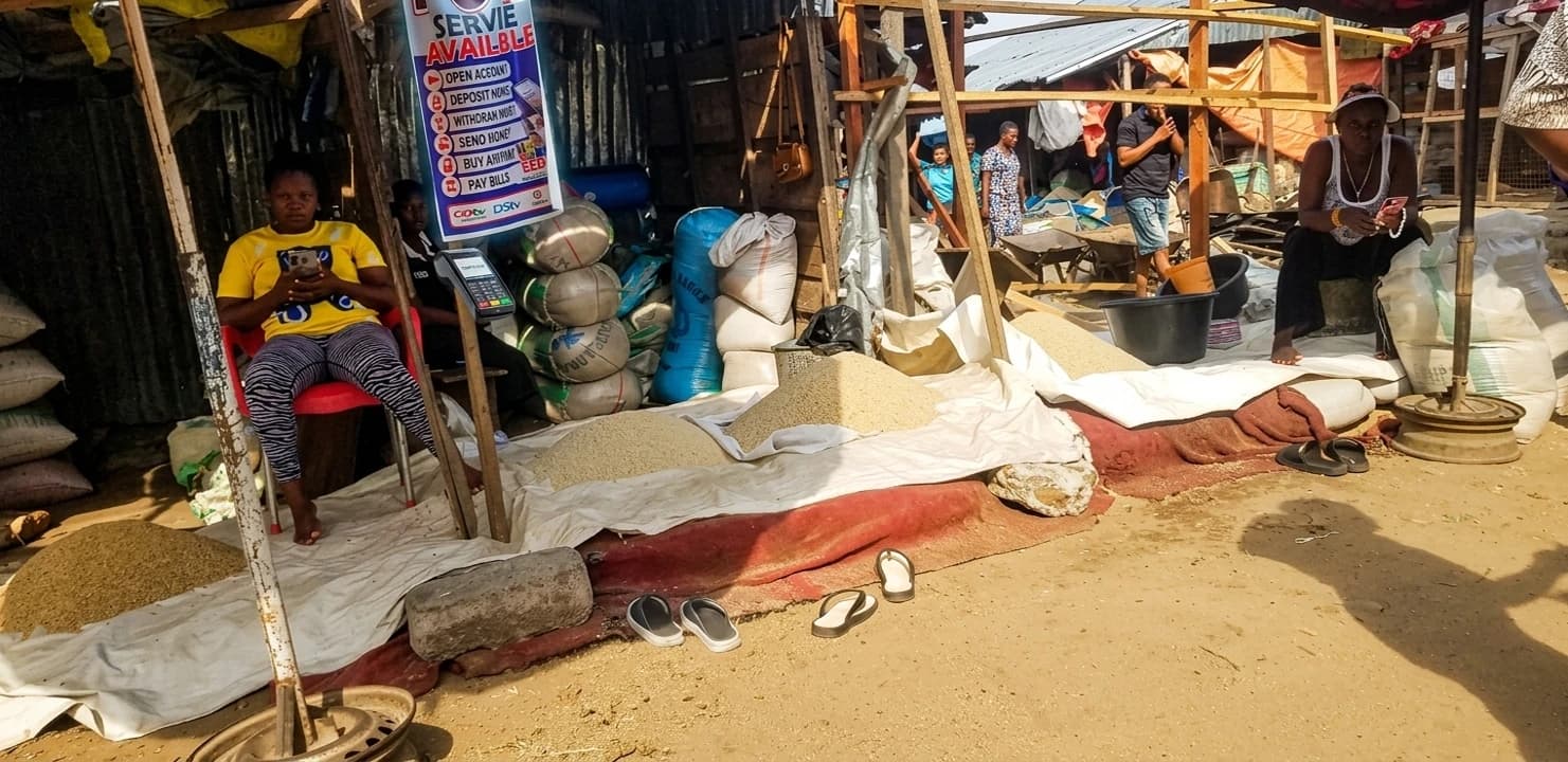 People buying and selling rice at a busy outdoor market stall.
