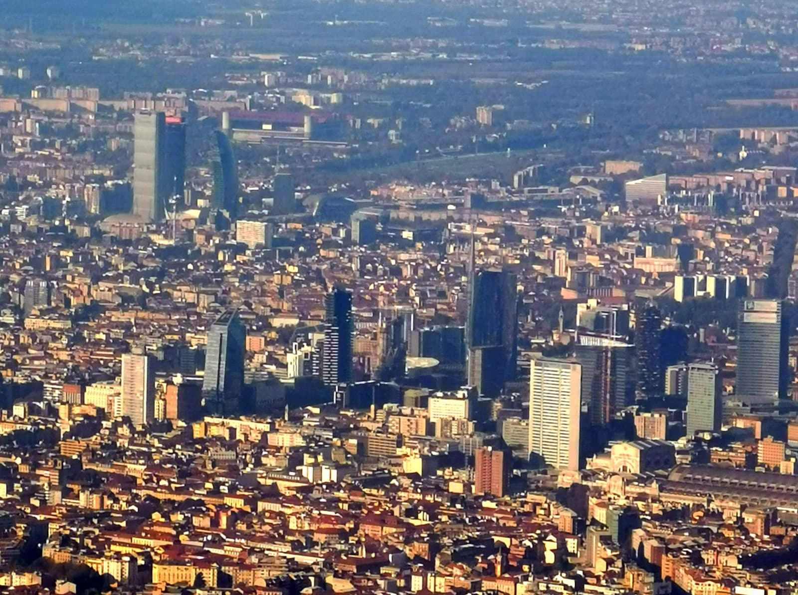 Aerial view of Milan, Italy, showing modern skyscrapers amidst a dense urban landscape.