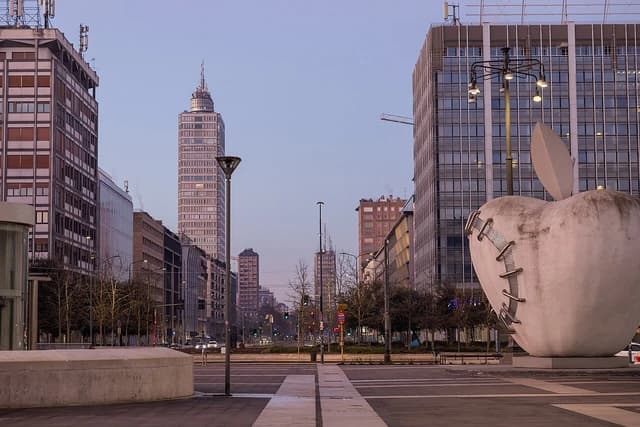 Piazza Duca d'Aosta in Milan featuring modern buildings and a prominent apple sculpture.