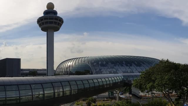 Jewel Changi Airport, with its distinctive domed roof and the airport control tower, against a cloudy sky.