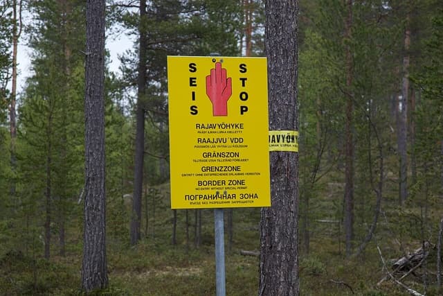 Border zone sign in multiple languages in a forest, including Finnish, Swedish, German, English, and Russian.