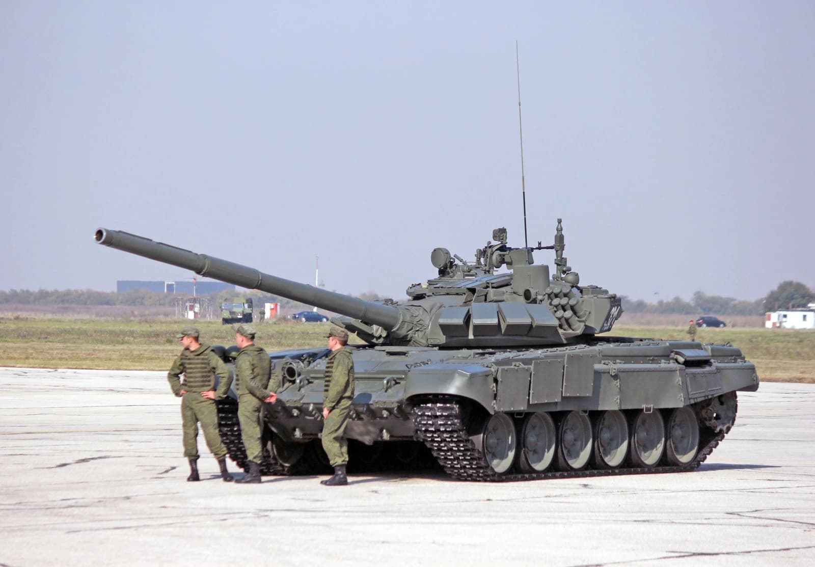 Three soldiers stand next to a Russian T-72 main battle tank on an airfield.
