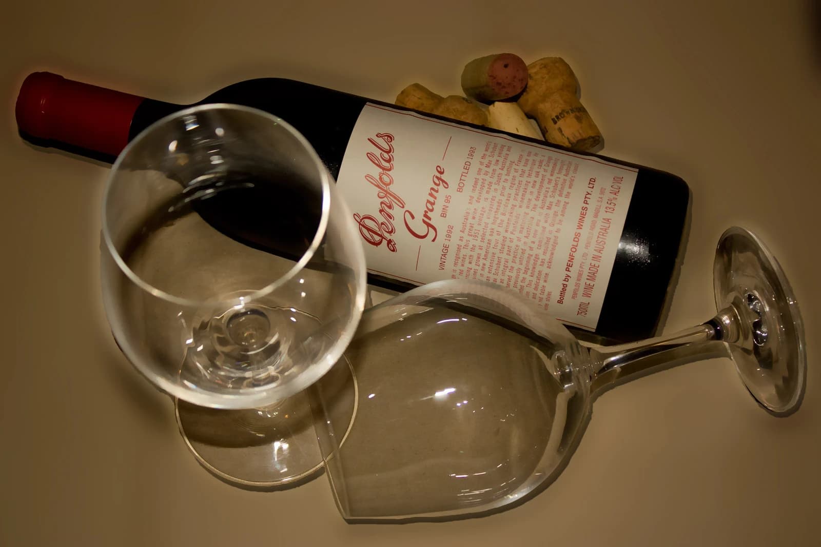 A Penfolds Grange wine bottle, two wine glasses, and wine corks rest on a surface.