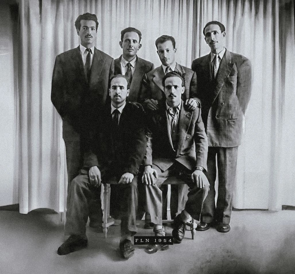 Six men, some standing and some sitting, posing for a group photograph.