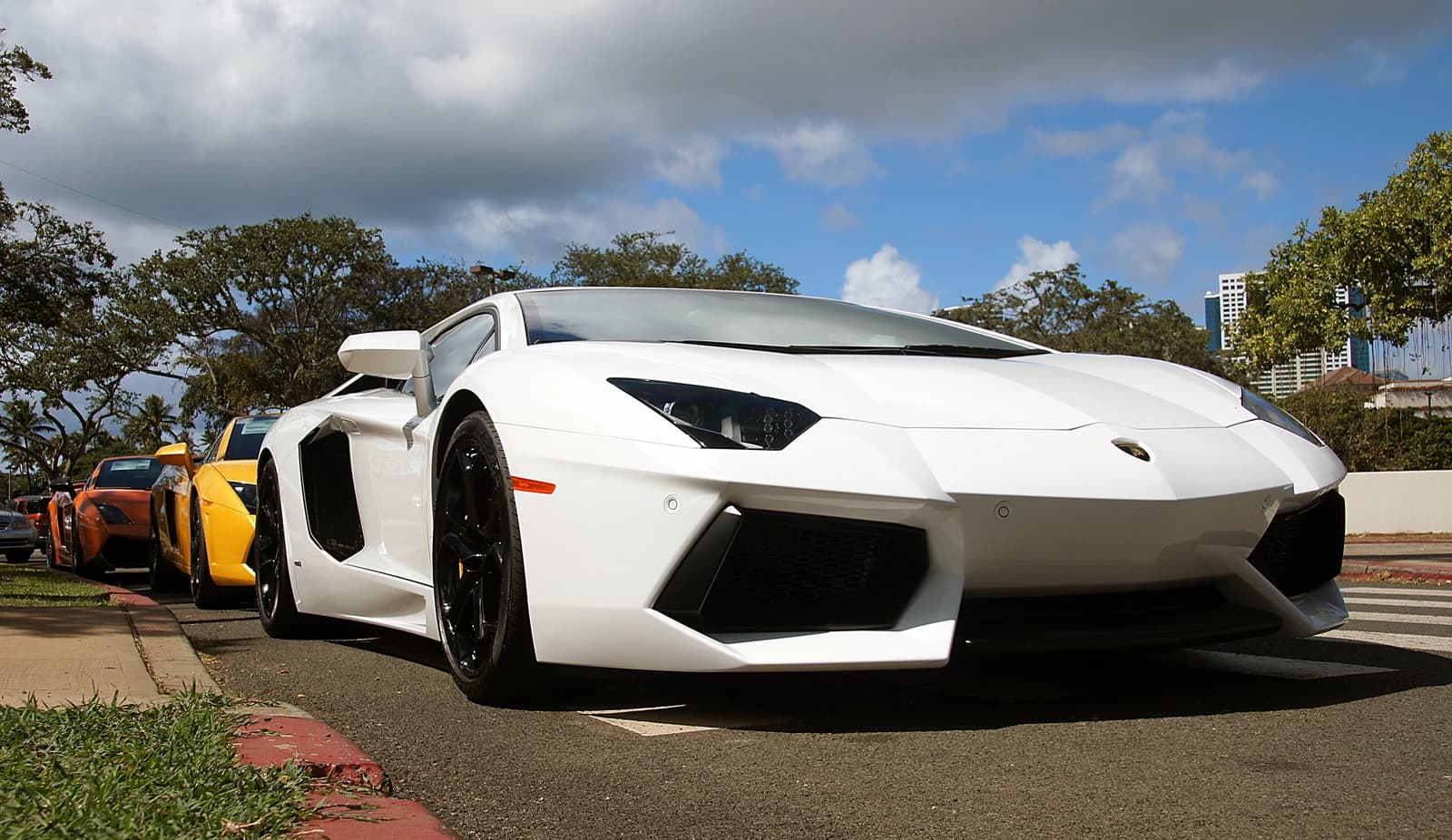 A white Lamborghini Aventador parked on a street, with other Lamborghinis behind it.