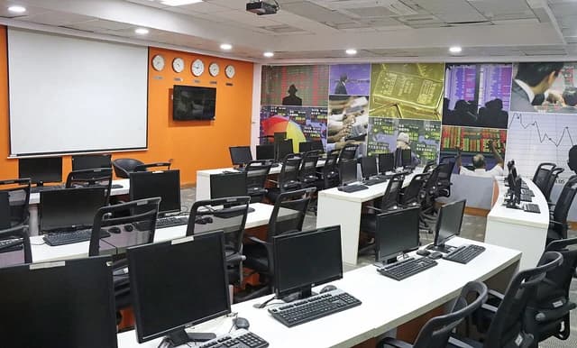 Financial trading room with rows of desks, computer monitors, and wall displays.