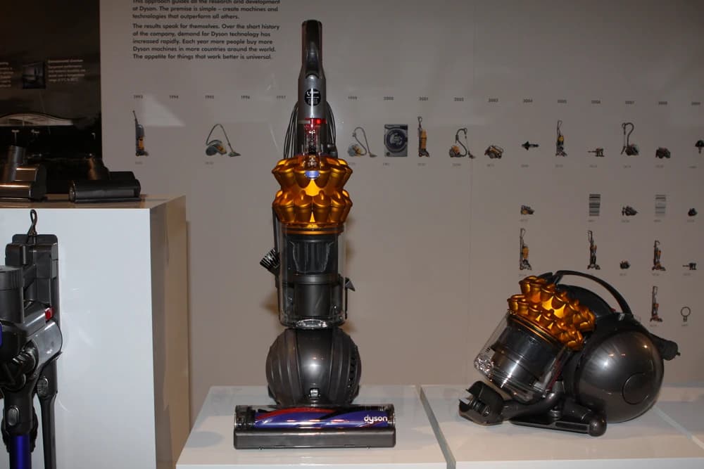 Dyson upright and canister vacuum cleaners displayed on white pedestals at a media launch event.