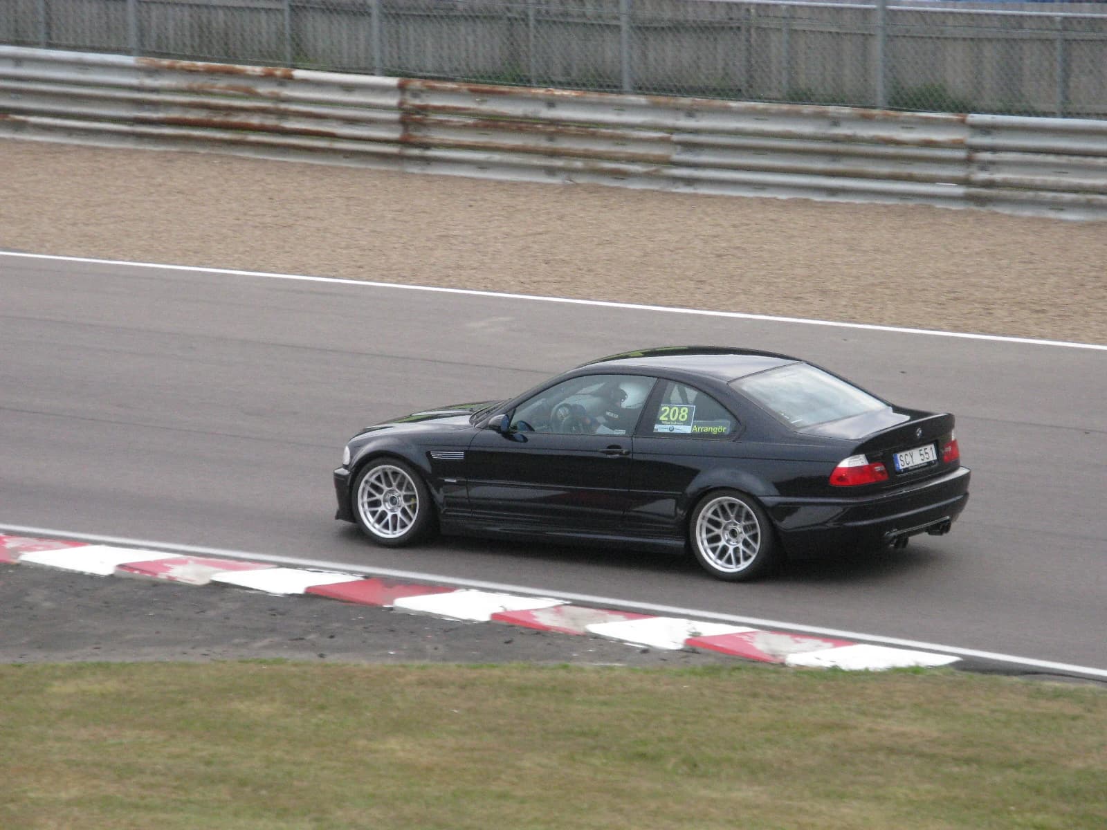 Black BMW M3 Coupé E46 driving on an asphalt race track during the day.
